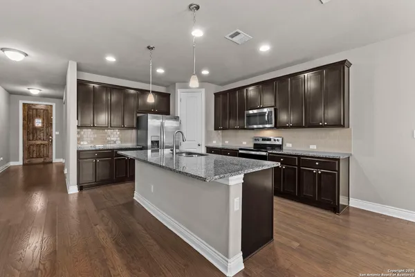 a kitchen with stainless steel appliances granite countertop wooden cabinets a refrigerator a stove a sink and a oven with wooden floors