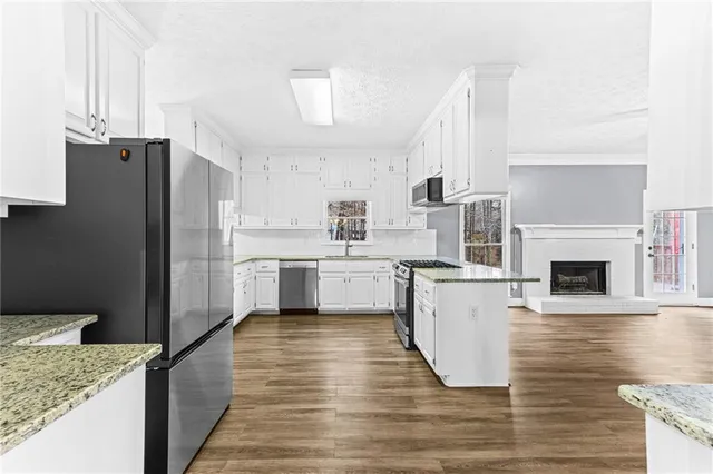 a kitchen with granite countertop a refrigerator a stove and white cabinets with wooden floor