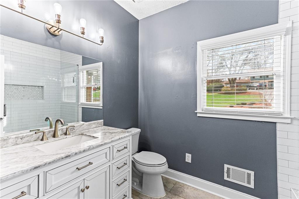 1394 Maple Drive Southwest Lilburn, GA 30047 - Photo 18 of 31 a bathroom with a granite countertop toilet a sink a mirror and a window