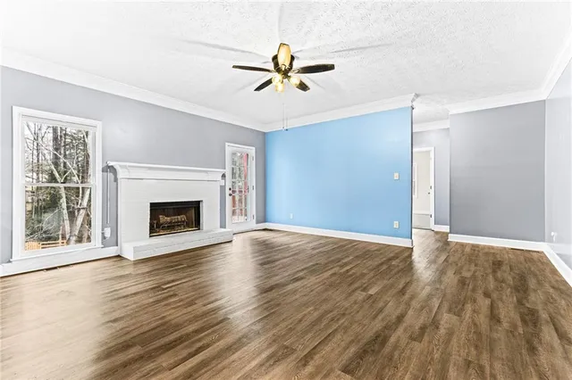 an empty room with wooden floor a ceiling fan a fireplace and windows