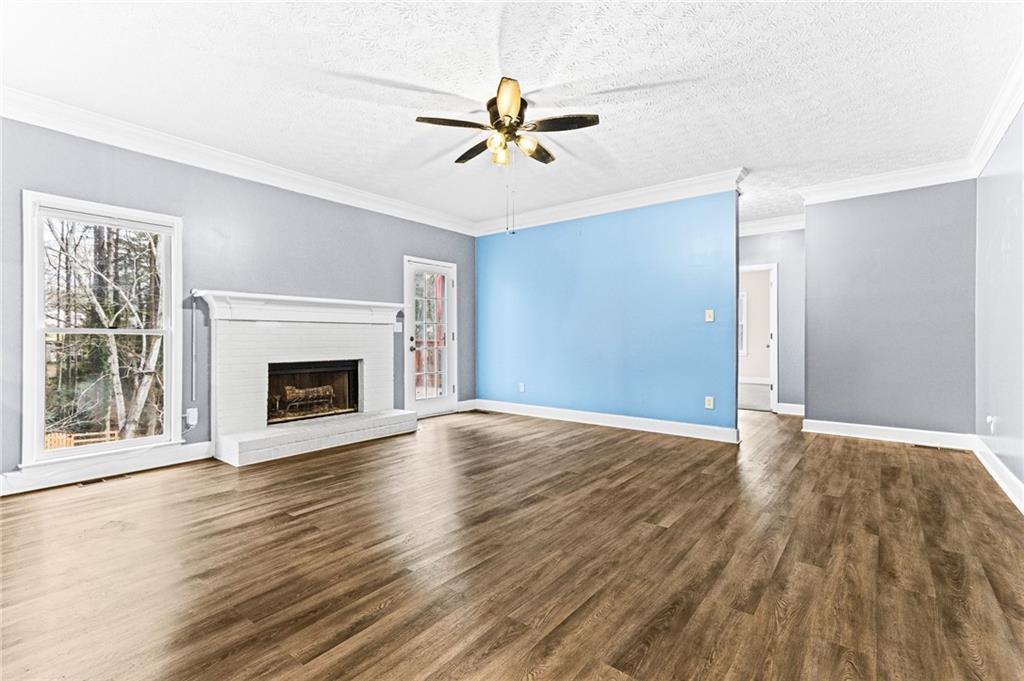 1394 Maple Drive Southwest Lilburn, GA 30047 - Photo 8 of 31 an empty room with wooden floor a ceiling fan a fireplace and windows