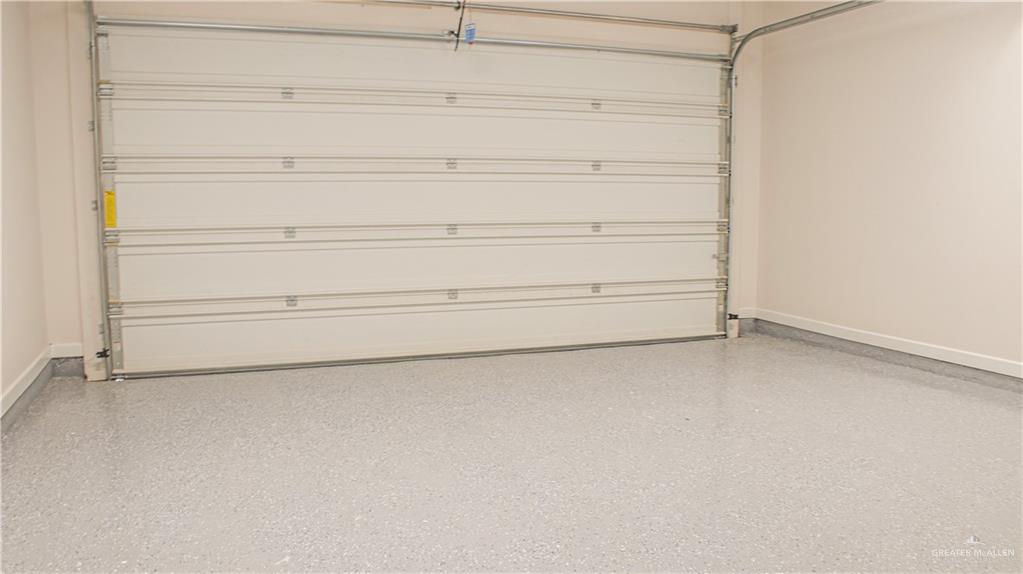 900 Azalea Street Mission, TX 78573 - Photo 8 of 12 Garage interior featuring a sectional overhead door, light beige painted walls, and an epoxy-coated concrete floor with a speckled finish