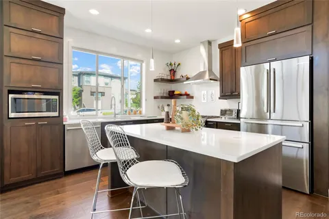 a kitchen with stainless steel appliances granite countertop a sink a stove a refrigerator with grey cabinets and wooden floor