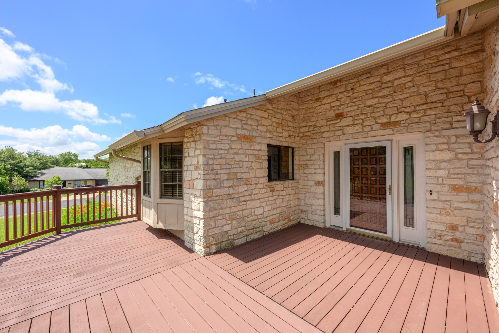 7210 Smokey Hill Road Austin, TX 78736 - Photo 3 of 29 A spacious wooden deck provides ample outdoor living space, complementing the home's sturdy stone exterior.