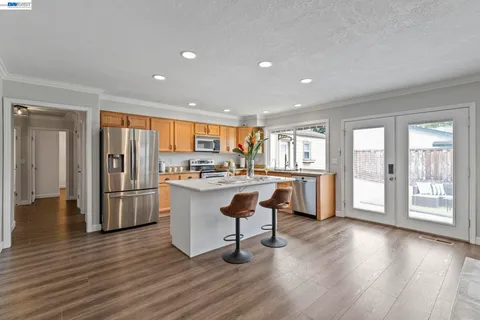 a room with kitchen island granite countertop wooden floors and stainless steel appliances