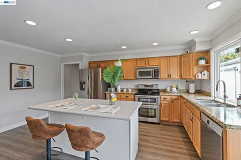 a kitchen with stainless steel appliances granite countertop a stove top oven a sink dishwasher a dining table and chairs with wooden floor