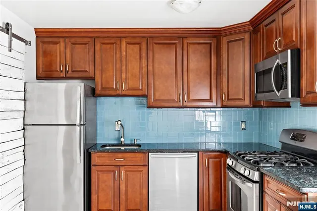 a kitchen with stainless steel appliances granite countertop a refrigerator stove top oven and granite countertops with wooden floor