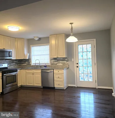 a kitchen with stainless steel appliances granite countertop a sink a stove a wooden floor and a window