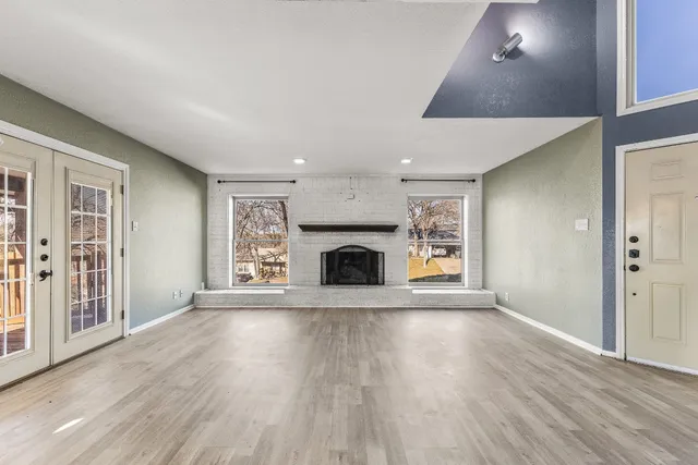 a view of an empty room with wooden floor fireplace and a window