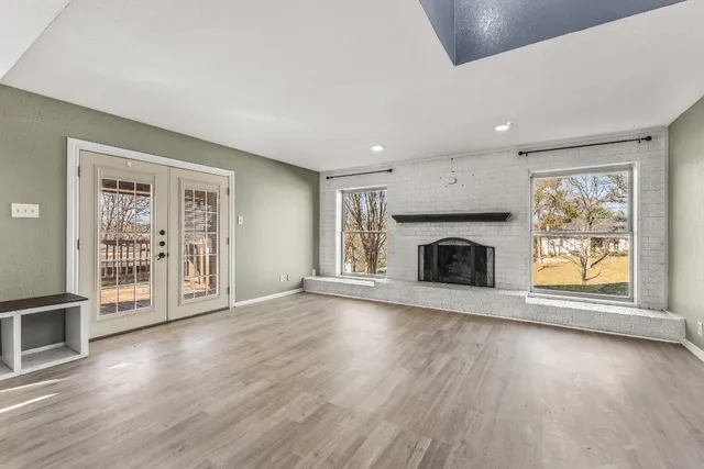 an empty room with wooden floor fireplace and windows