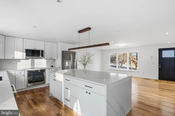 a kitchen with stainless steel appliances granite countertop a sink dishwasher a refrigerator and white cabinets with wooden floor