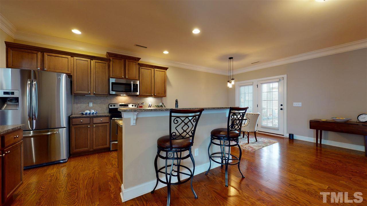 628 Democracy Street Raleigh, NC 27603 - Photo 9 of 26 a kitchen with granite countertop stainless steel appliances a refrigerator a stove a dining table and chairs with wooden floor
