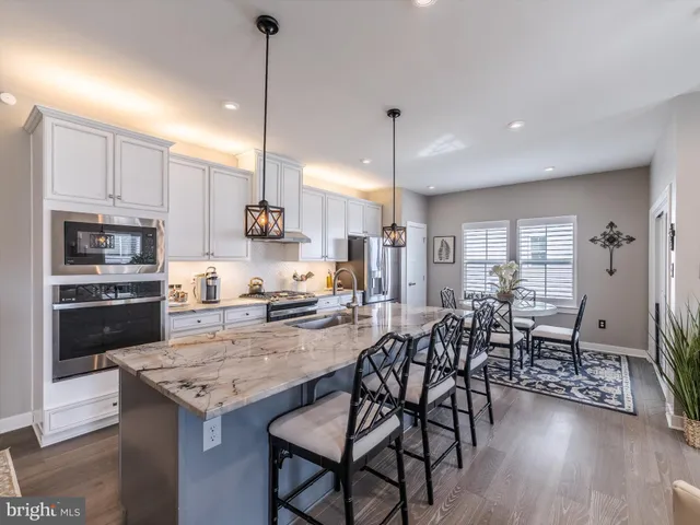 a kitchen with stainless steel appliances kitchen island granite countertop a stove a refrigerator a kitchen island a dining table and chairs with wooden floor