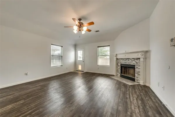 an empty room with wooden floor fireplace and windows