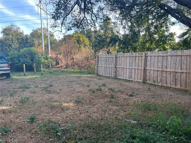 a view of a backyard with large trees and wooden fence