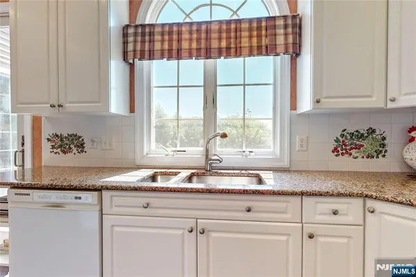 a white kitchen with granite countertop white cabinets and a window