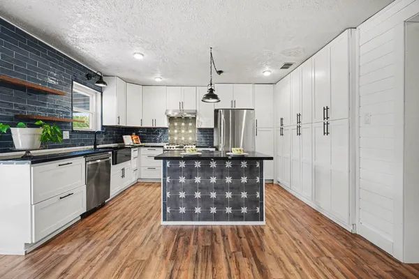 a kitchen with stainless steel appliances granite countertop a refrigerator a sink dishwasher a stove and white countertops with wooden floor