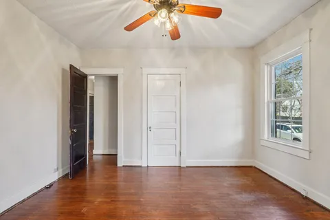 an empty room with wooden floor chandelier fan and windows