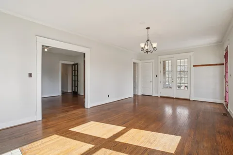 an empty room with wooden floor chandelier and windows