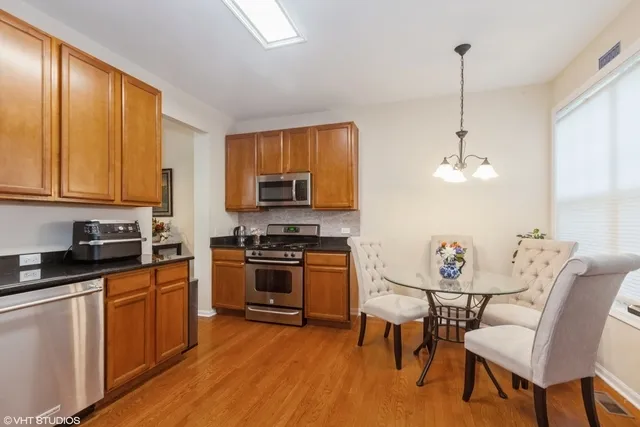 a kitchen with stainless steel appliances granite countertop a stove top oven a sink a dining table and chairs with wooden floor