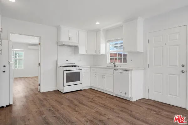 a kitchen with a hard wood floor white cabinets and white appliances