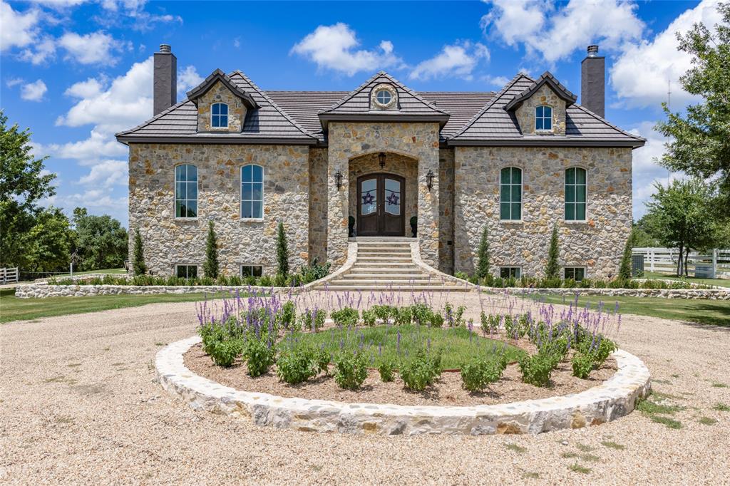 501 Upper Denton Road Weatherford, TX 76085 - Photo 2 of 40 Stone facade with a multi-level roofline, arched entry, dormer windows, and a circular gravel driveway featuring a landscaped island
