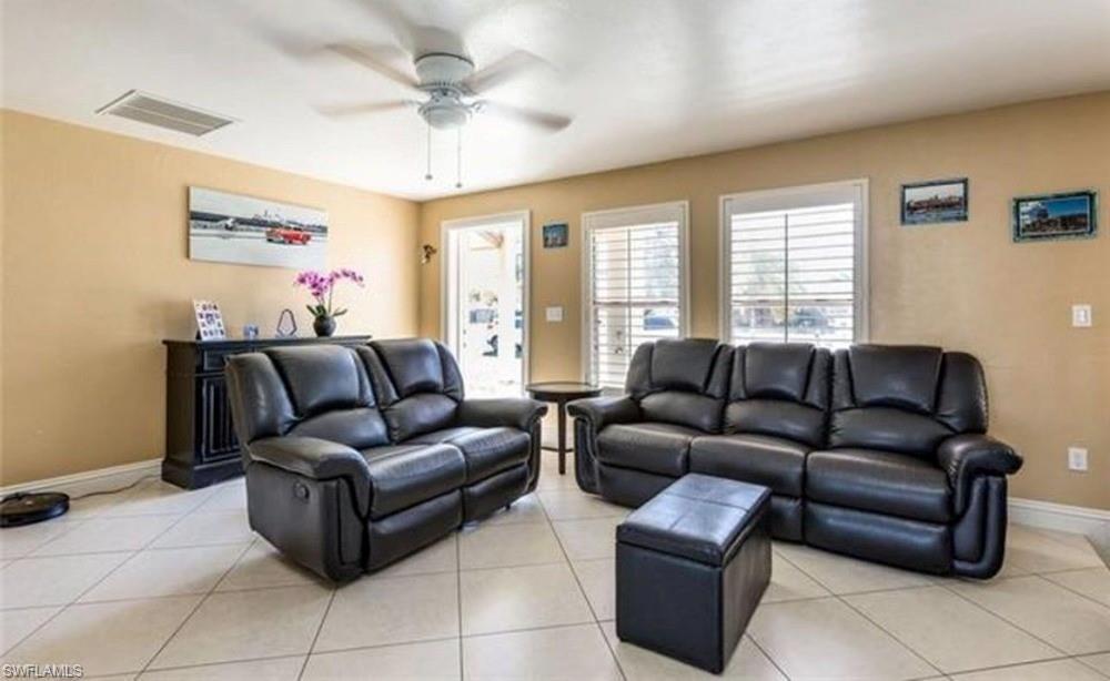 5325 23rd Place Southwest Naples, FL 34116 - Photo 4 of 10 Spacious living area featuring light-toned tiled flooring, neutral wall tones, multiple windows with white plantation shutters, and a ceiling fan with integrated lighting
