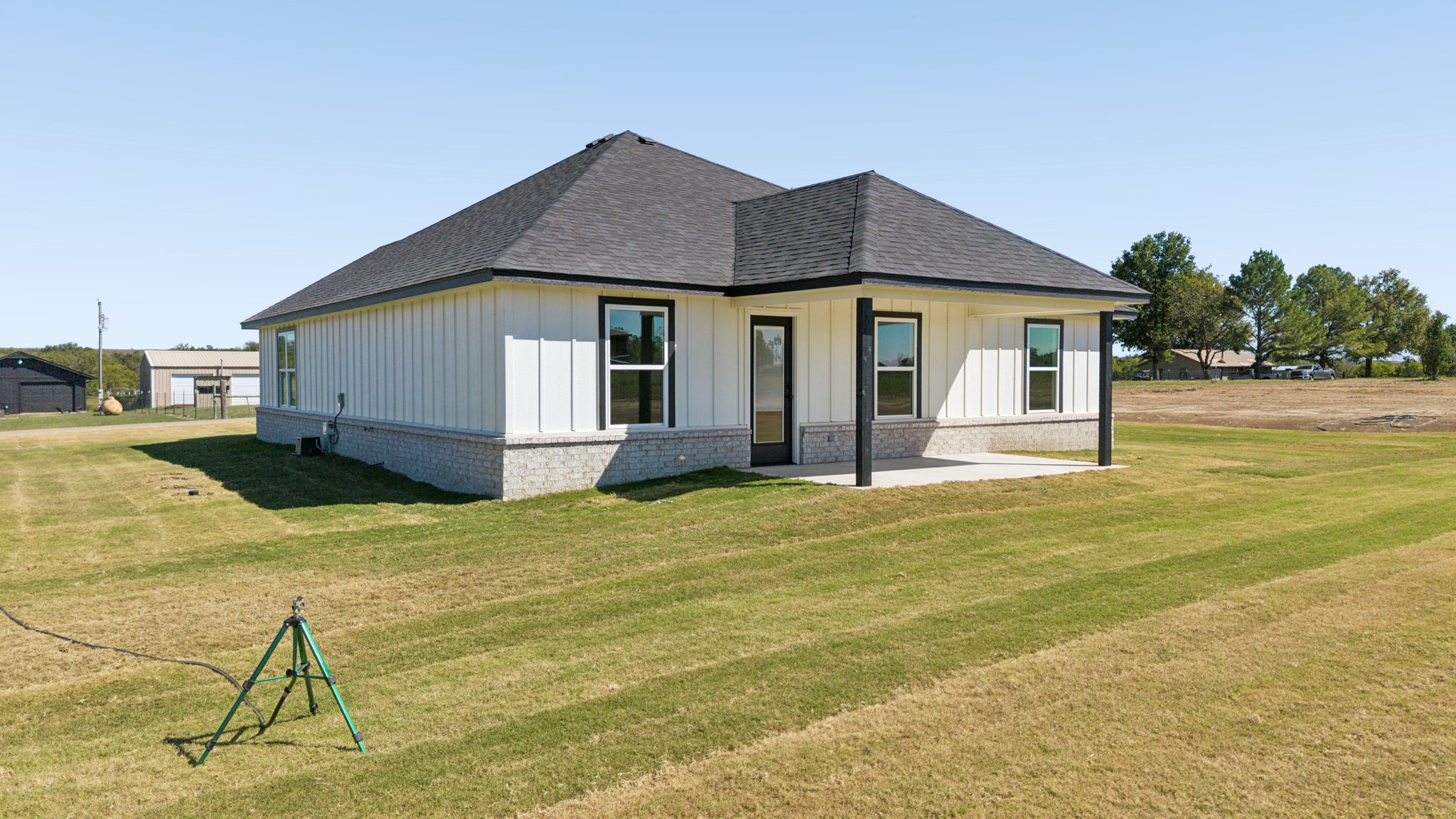 25036 South 4205 Road Inola, OK 74036 - Photo 26 of 30 White vertical siding exterior with a dark shingle roof, black-framed windows, and a covered patio
