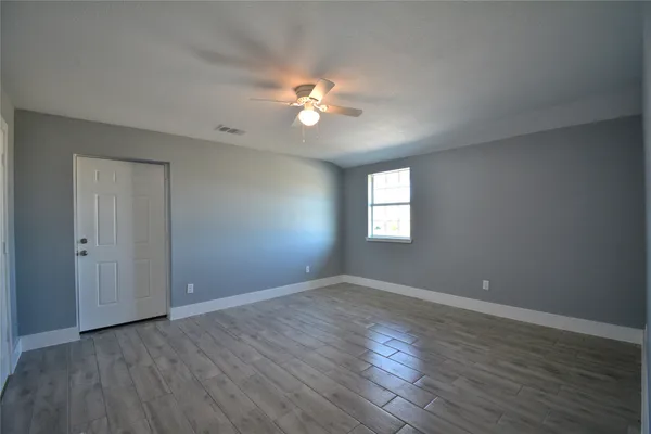 a view of empty room with wooden floor and fan
