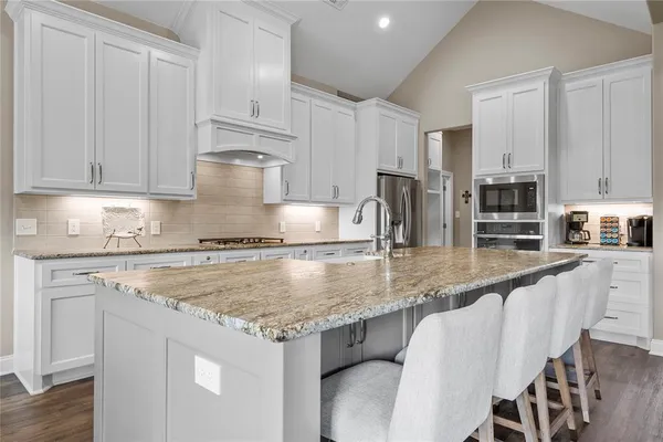 a kitchen with stainless steel appliances granite countertop a stove top oven a sink and white cabinets