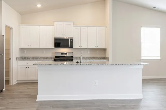 a white kitchen with granite countertop white cabinets and stainless steel appliances