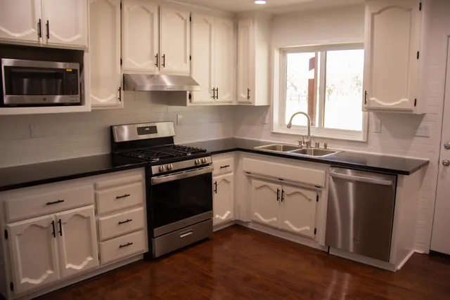 a kitchen with granite countertop white cabinets white stainless steel appliances and a sink
