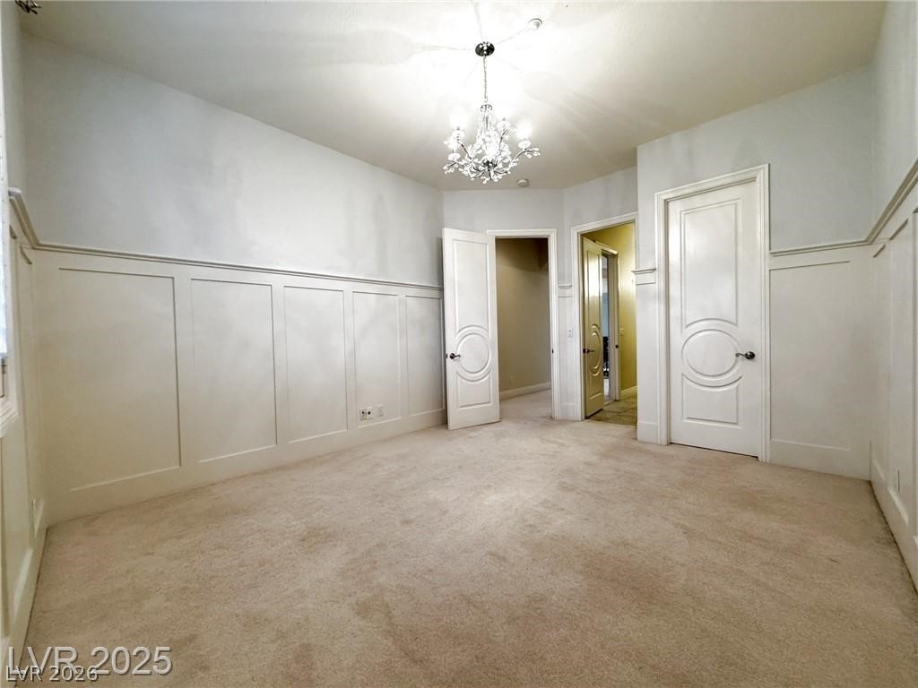 861 Majestic Ridge Court Henderson, NV 89052 - Photo 46 of 68 Unfurnished bedroom with a decorative wall, a chandelier, wainscoting, and light colored carpet