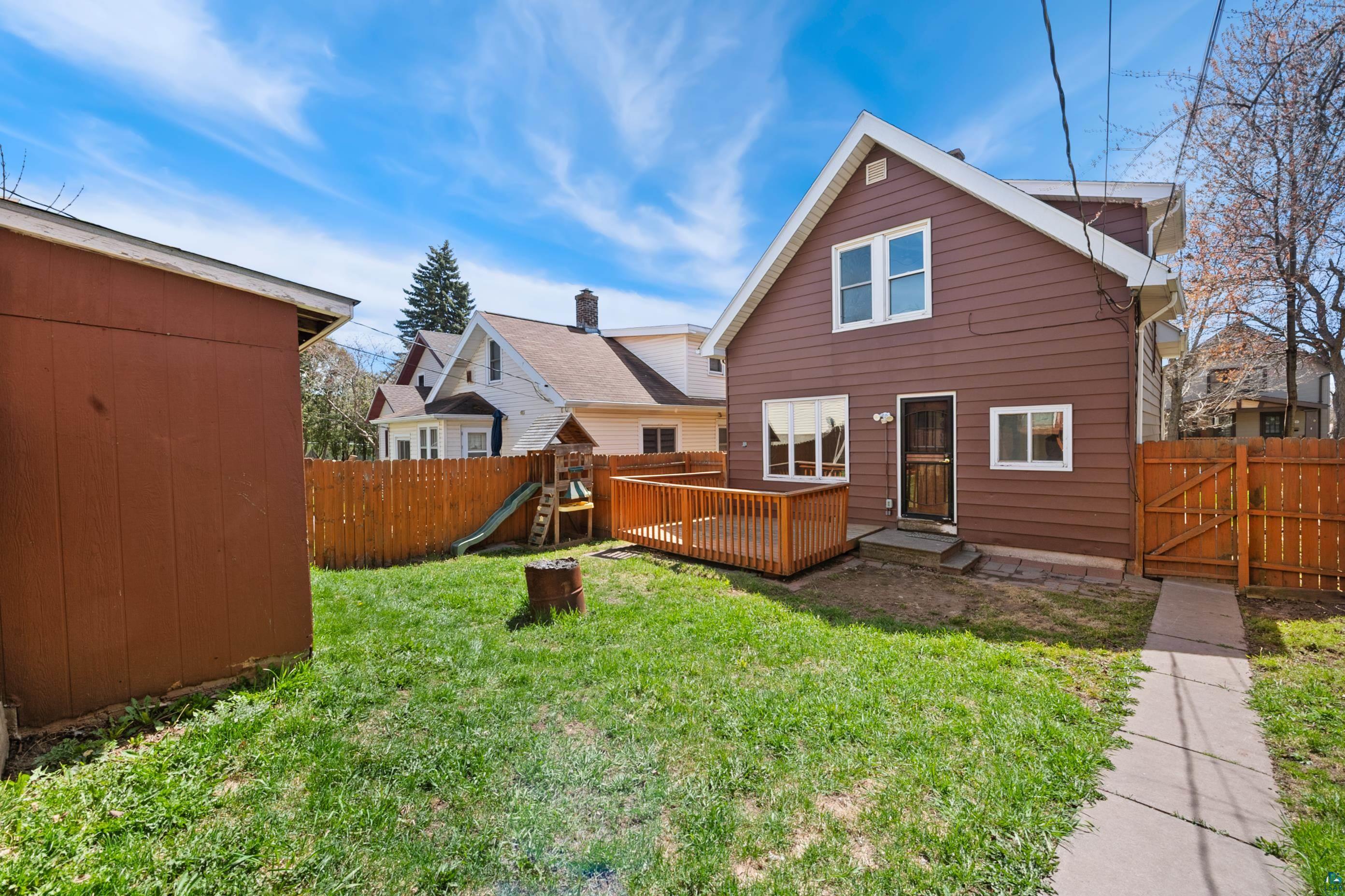 3067 Restormel Street Duluth, MN 55806 - Photo 25 of 25 Expansive backyard featuring a manicured lawn, a brown wood-paneled storage shed, a wooden privacy fence, a wooden deck, and a concrete pathway
