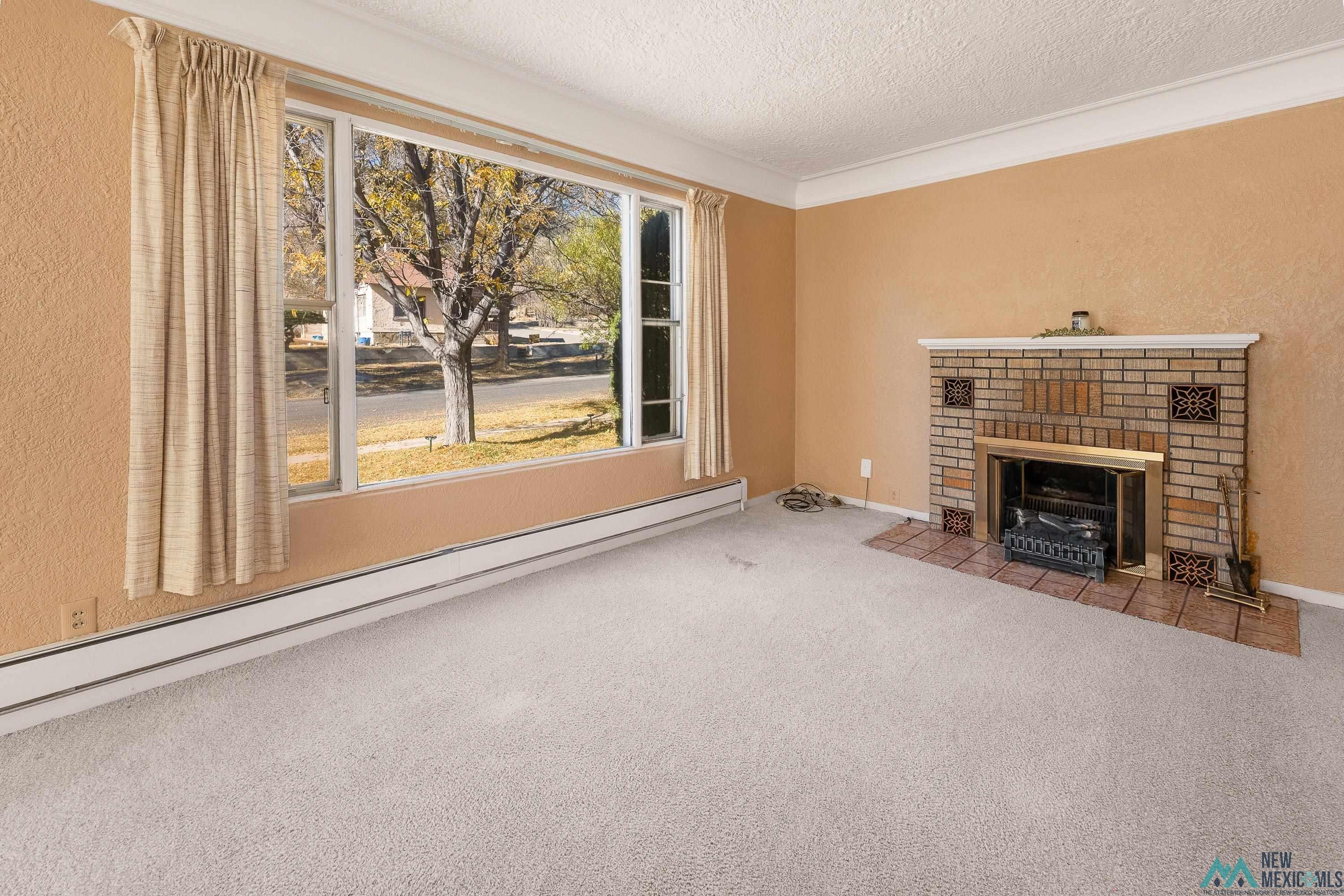 727 South 6th Street Raton, NM 87740 - Photo 4 of 47 Unfurnished living room featuring baseboard heating, carpet flooring, a brick fireplace, a textured ceiling, and a textured wall
