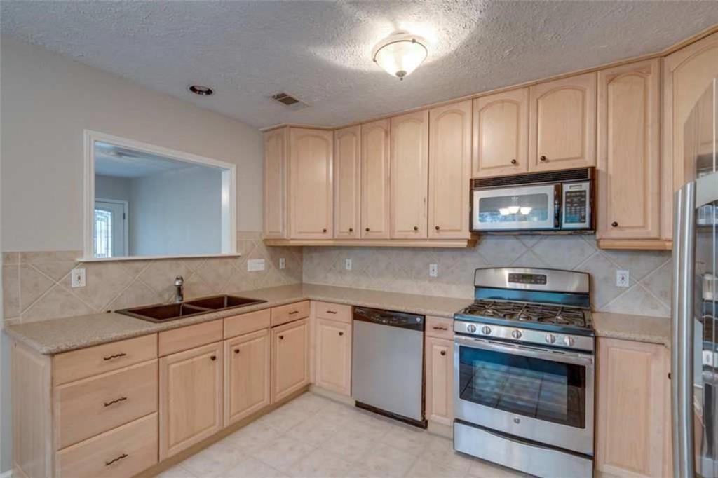 2802 South 4th Street Austin, TX 78704 - Photo 11 of 27 Kitchen with appliances with stainless steel finishes, light brown cabinetry, a textured ceiling, light floors, and light stone countertops **NOTE: Microwave no longer available, it has been relaced with a vent**