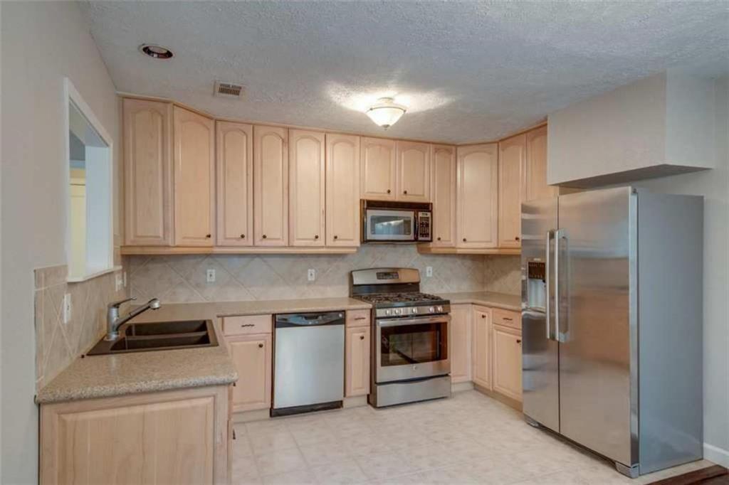 2802 South 4th Street Austin, TX 78704 - Photo 10 of 27 Kitchen featuring stainless steel appliances, light brown cabinetry, decorative backsplash, light stone countertops, and a textured ceiling. **NOTE: Microwave no longer available, it has been relaced with a vent**