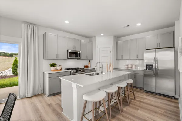 a kitchen with stainless steel appliances a stove a sink a refrigerator white cabinets and wooden floor