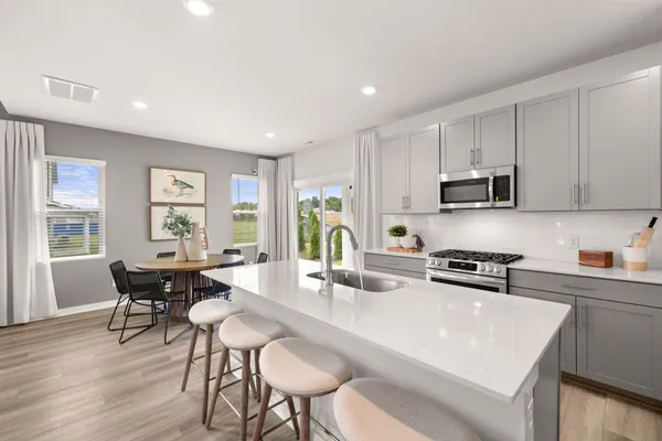a kitchen with stainless steel appliances granite countertop a stove a sink a microwave a dining table and chairs with wooden floor