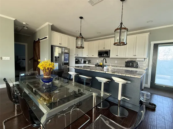a kitchen with stainless steel appliances granite countertop a stove a refrigerator a sink a dining table and chairs with the wooden floor