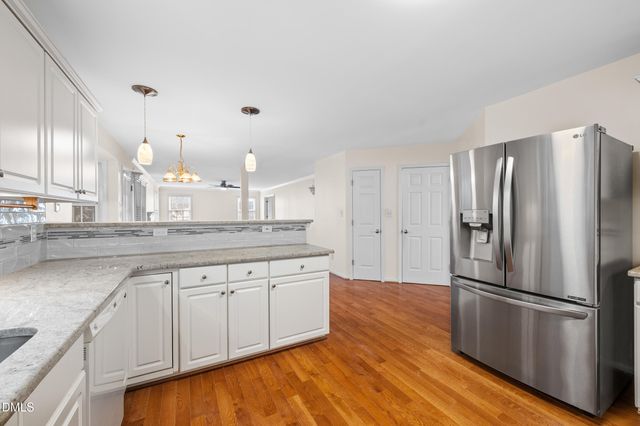 a kitchen with stainless steel appliances granite countertop a refrigerator a sink and white cabinets with wooden floor