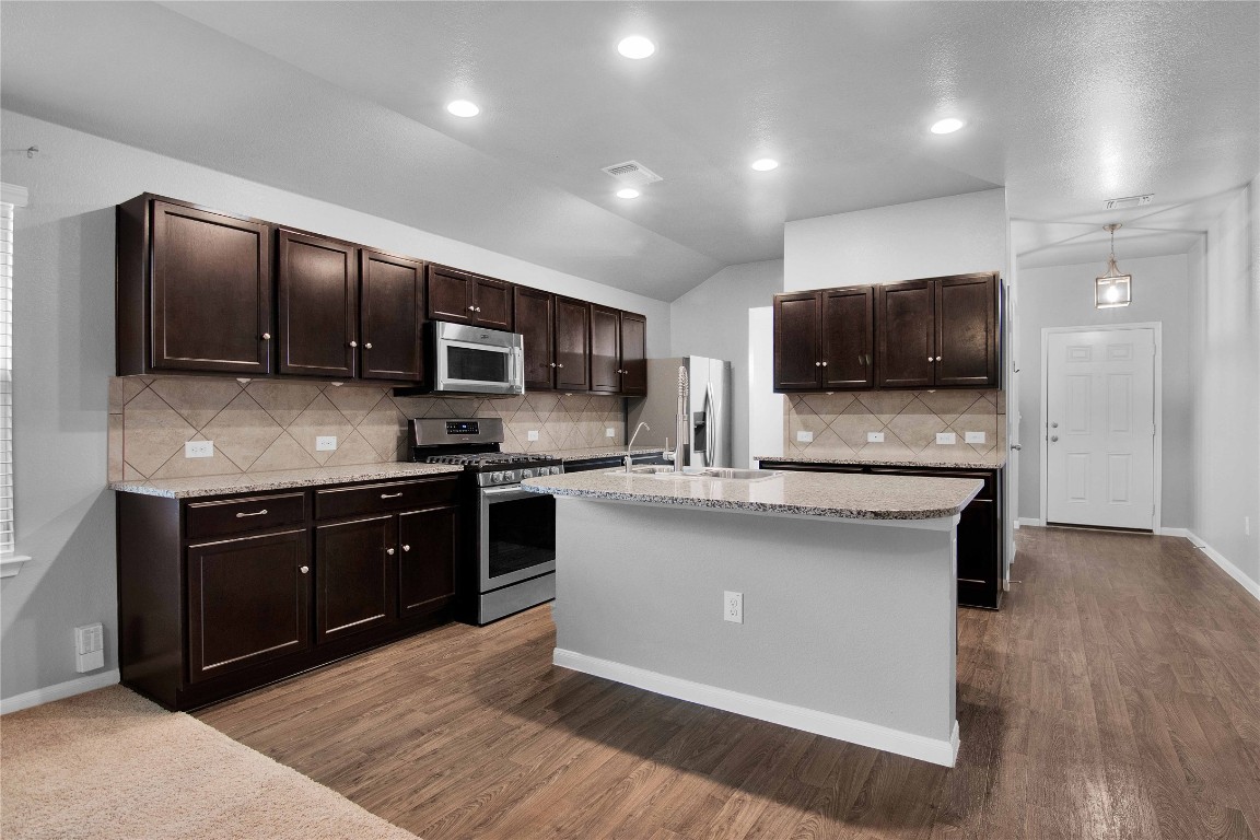 704 Red Tails Drive Austin, TX 78725 - Photo 11 of 37 a kitchen with stainless steel appliances granite countertop a stove a sink dishwasher a microwave oven and a refrigerator with wooden floor