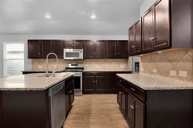 a kitchen with stainless steel appliances granite countertop a stove a sink dishwasher a microwave oven and a refrigerator with wooden floor