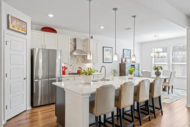 a kitchen with stainless steel appliances granite countertop a refrigerator a sink dishwasher a dining table and chairs with wooden floor