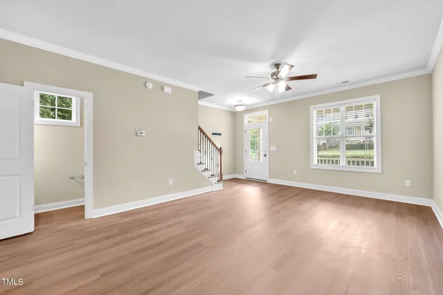 an empty room with wooden floor chandelier fan and windows