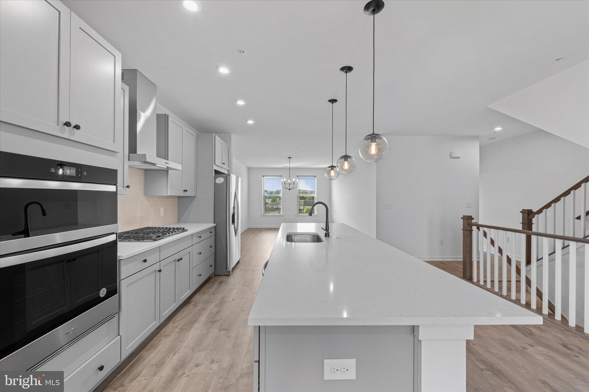 46207 Woodpecker Square Sterling, VA 20165 - Photo 7 of 37 a large kitchen with kitchen island a stove a sink a refrigerator and white cabinets with wooden floor