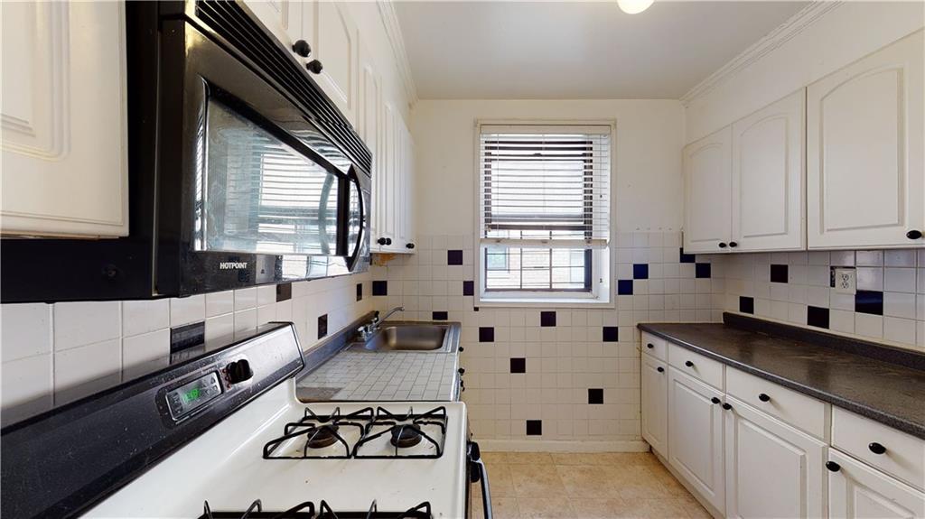 150 West End Avenue, Unit 5H Brooklyn, NY 11235 - Photo 4 of 17 a large white kitchen with granite countertop a sink a stove a window and white cabinets