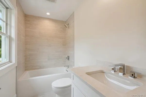 a bathroom with a bathtub shower sink vanity mirror and toilet