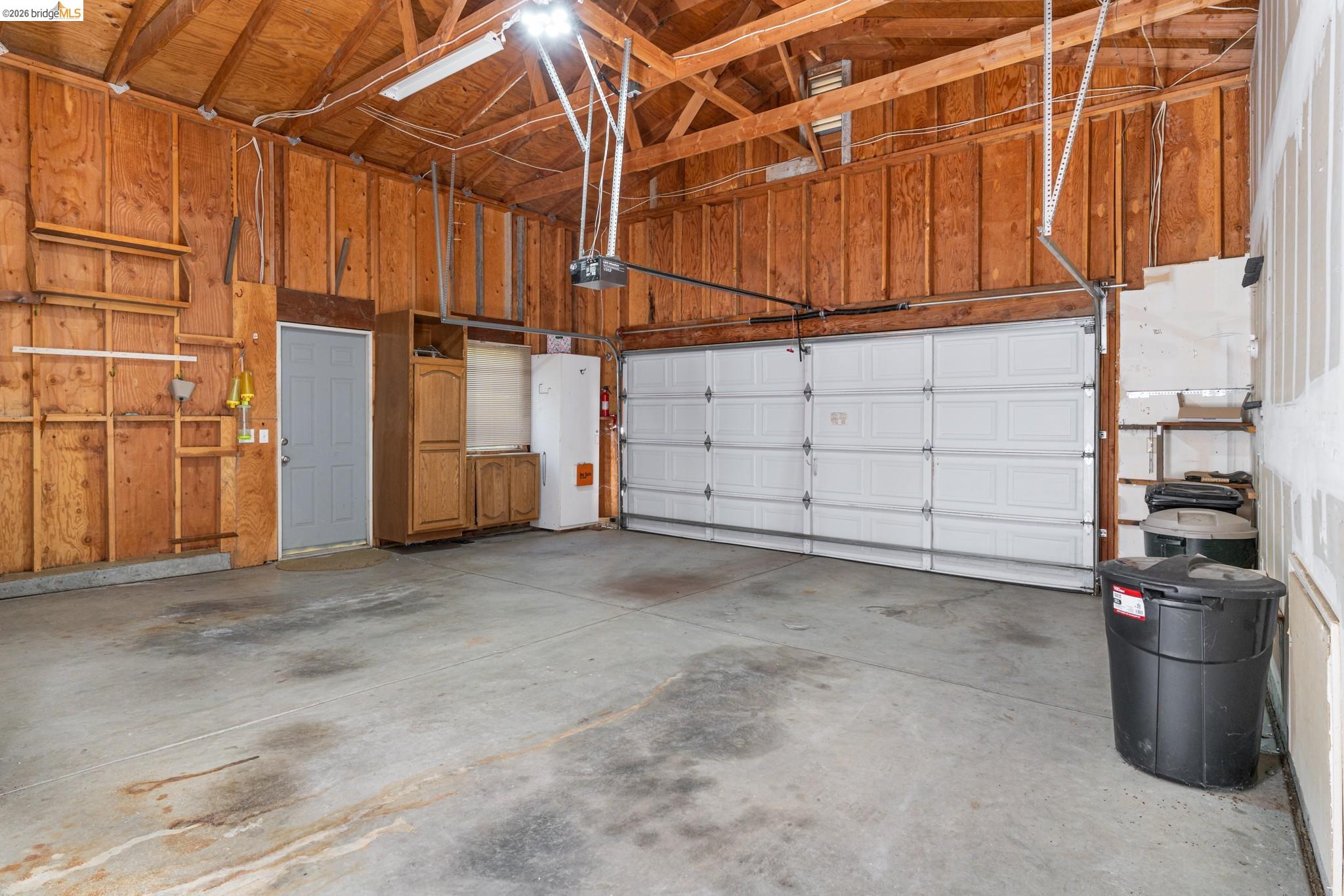 19390 Ferretti Road Groveland, CA 95321 - Photo 30 of 38 Concrete flooring, wood-paneled walls, exposed ceiling beams, built-in wooden cabinetry, white garage door