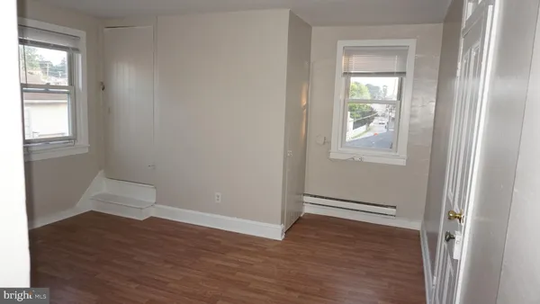 an empty room with wooden floor closet and windows